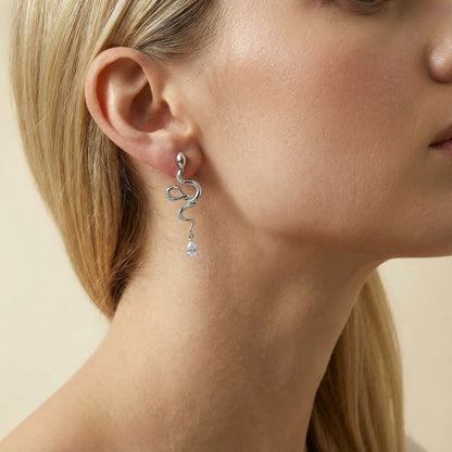 Close-up of a person wearing a silver earring with a clear gemstone on a neutral background