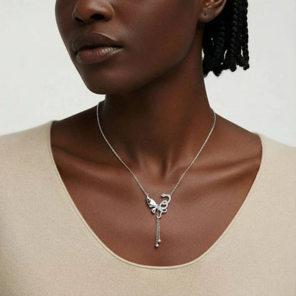 Woman wearing a silver necklace with a butterfly pendant on a plain background